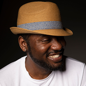 Headshot of Michael Morgan wearing a hat and smiling, against black background