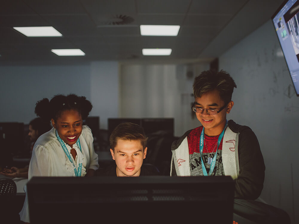 Three students standing in front of a computer in a classroom studio