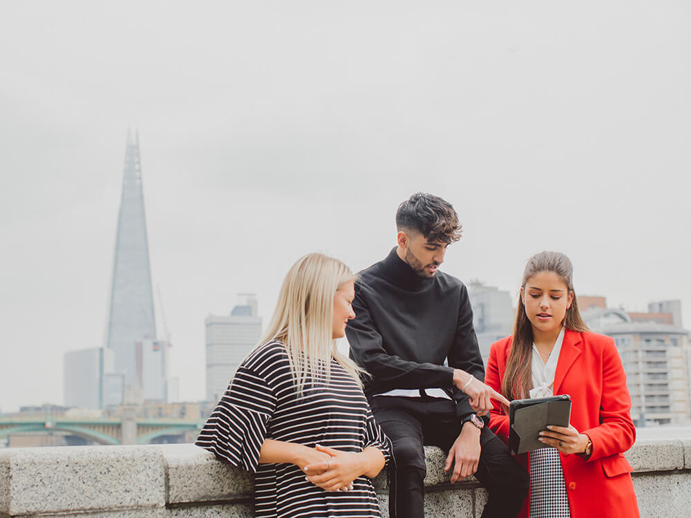 Group of students looking at iPad with London skyline background