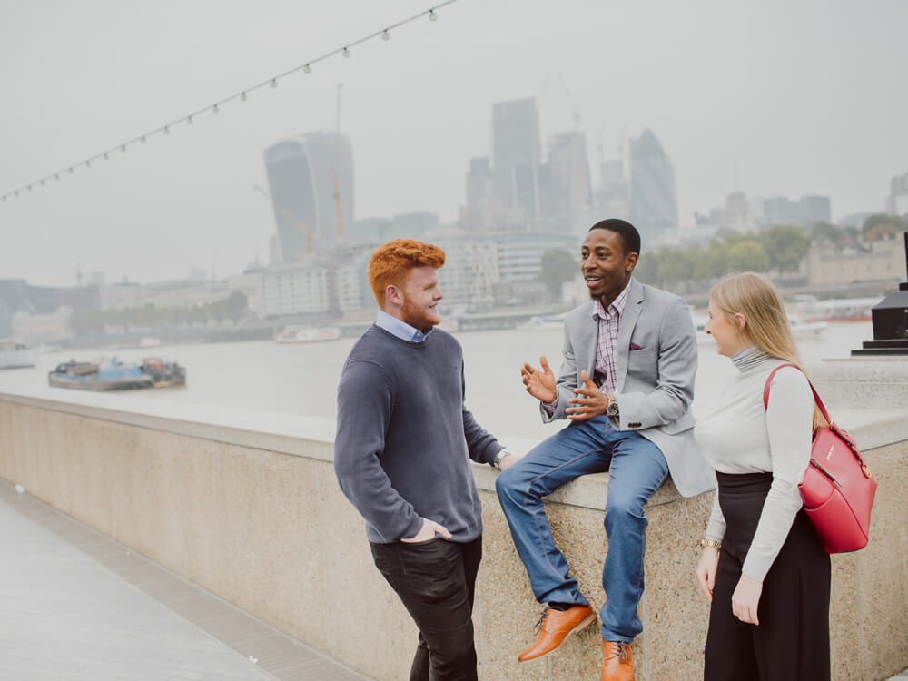 Three students talking with the London skyline in the background