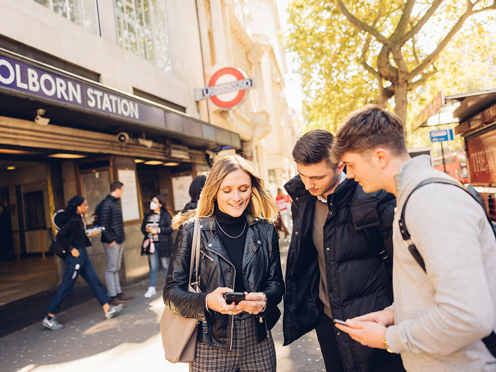 Three students looking at a phone outside Holborn tube station