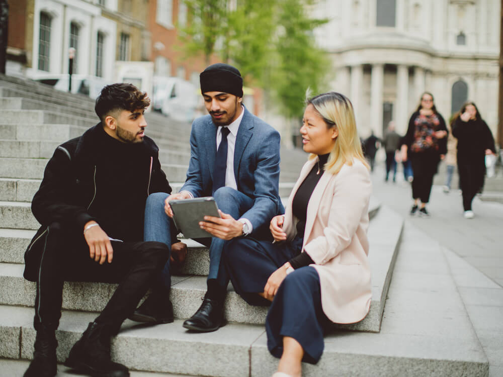 Three students sat on steps outside St Paul's cathedral and looking at a tablet