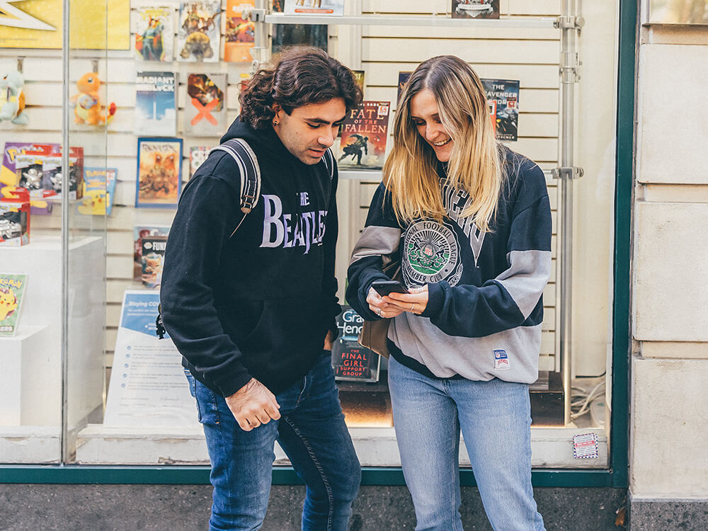 Two students looking at a mobile phone outside a shop