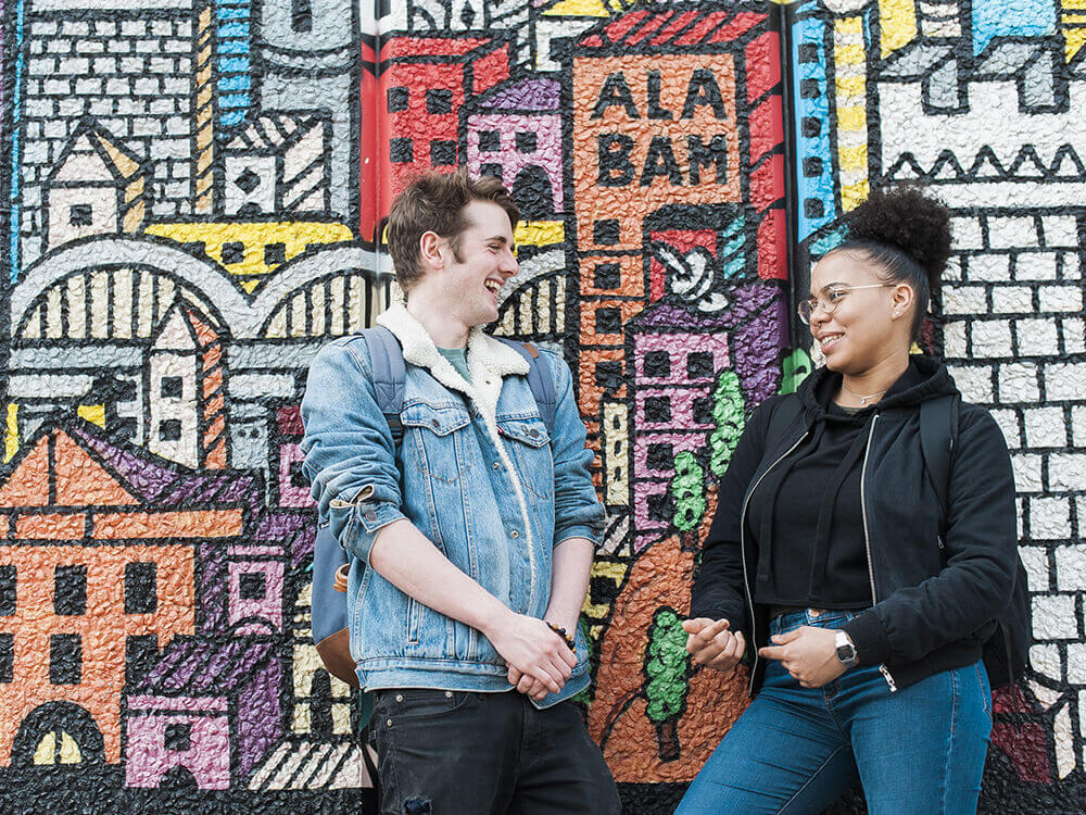 Two students talking in front of a colourful wall